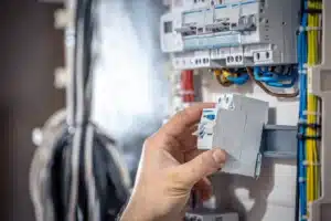 A male electrician connects cables in a switchboard, highlighting the importance of hiring qualified professionals.