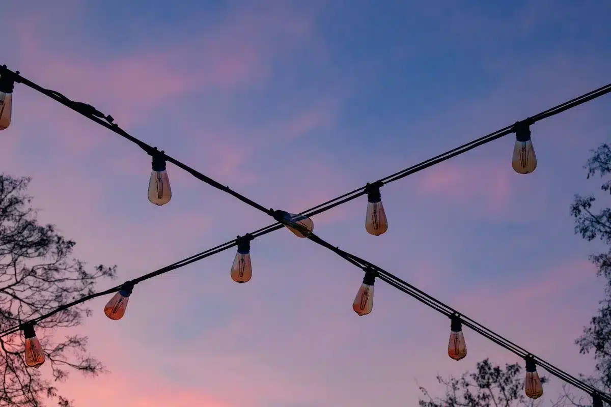 Outdoor string lights illuminate a colorful dusk sky, highlighting the importance of electrical work.