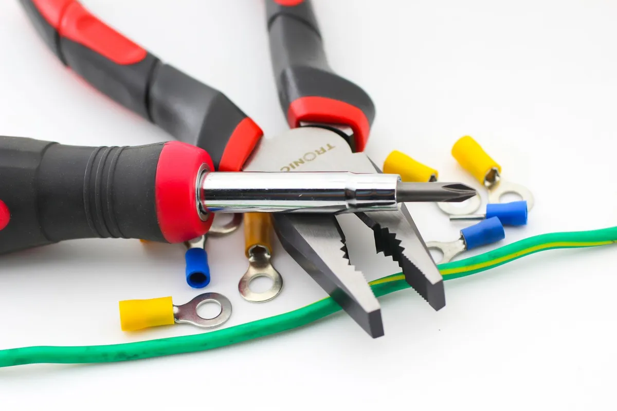 Close-up of pliers and screwdriver with colorful wire connectors on a white background, tools for electricians.